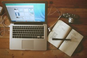 Laptop, headphones, notebook and camera on a wooden table.
