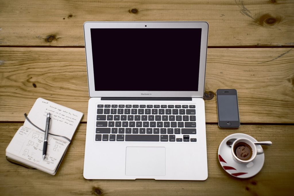 A laptop next to a notebook and some coffee.