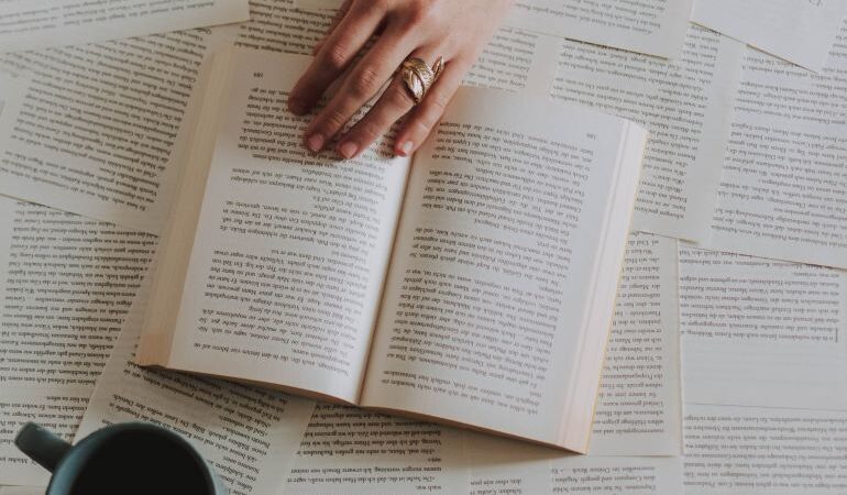 Dozens of open books, with a coffee mug.