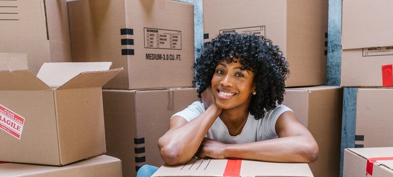 A happy woman sitting behind moving boxes and smiling.